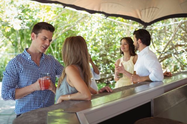 Group of friends enjoying drinks and conversation at an outdoor restaurant bar. Ideal for use in lifestyle blogs, social media posts, advertisements for restaurants or bars, and promotional materials for social events.