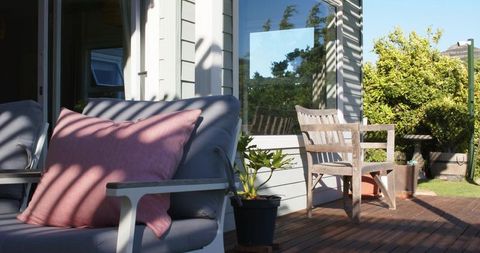 Sunlit outdoor deck lounge with grey cushioned sofa and pink throw pillow
