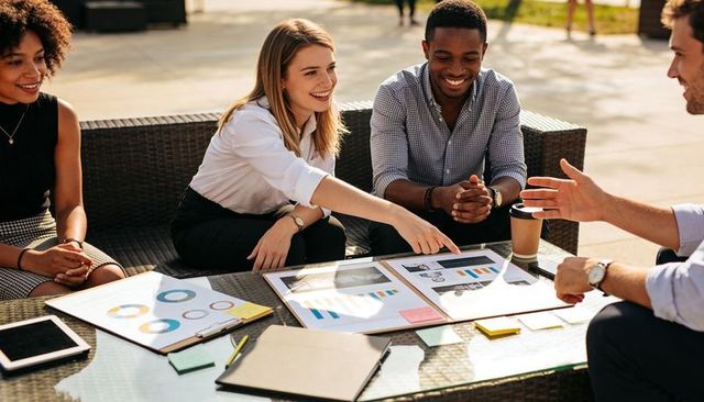 Team reviewing printed reports outdoors on patio pointing at charts during casual meeting