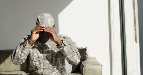 Soldier sitting thoughtfully on couch adjusting cap indoors