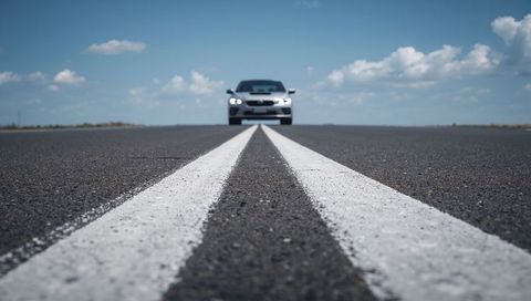 Low Angle Driving Silver Sedan on Open Highway with Double Centerlines and Headlights On