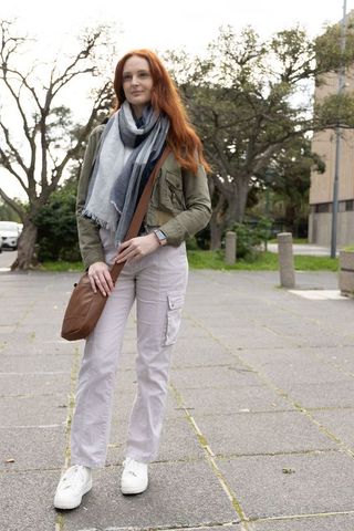 Red-haired woman standing on urban plaza wearing layered casual outfit with checked scarf