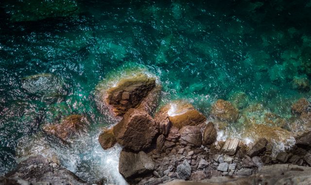 Capturing an picturesque landscape of a rocky coastline with clear, turquoise waters from an overhead perspective. Ideal for travel brochures, websites focusing on coastal tourism, nature-themed calendars, and environmental campaigns.