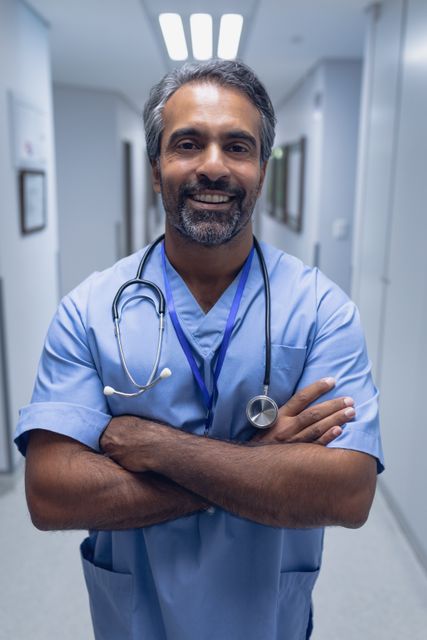 Male doctor standing confidently with arms crossed in a hospital corridor. Perfect for illustrating healthcare, medical professionalism, and hospital environments. Suitable for use in health blogs, medical articles, and healthcare promotional materials.