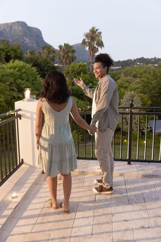 Young man gesturing while holding hands with asian woman on balcony at golden hour