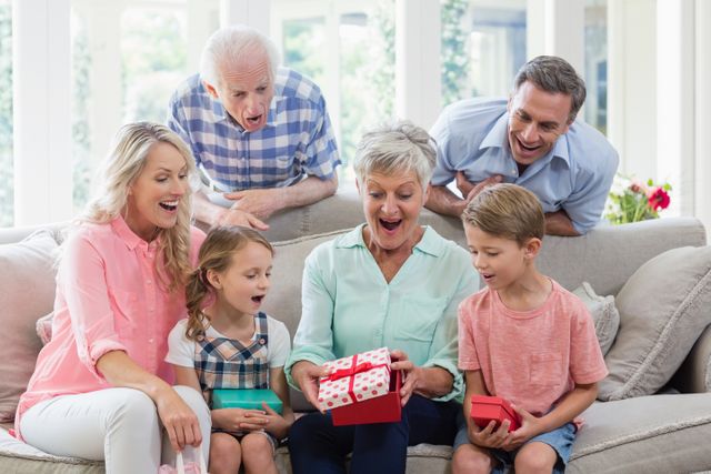 Multi-generational family gathered in living room, excitedly opening gifts. Perfect for themes of family bonding, celebrations, holidays, and joyful moments at home. Ideal for advertisements, greeting cards, and family-oriented content.
