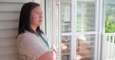 Mature Asian woman standing by sliding door looking contemplative on sunny porch