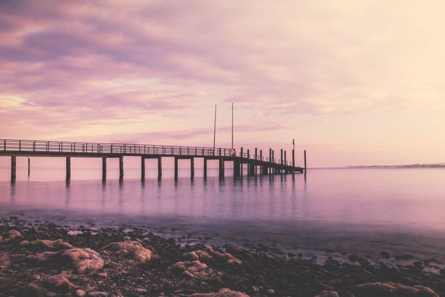 Silhouette of peaceful pier reaching towards horizon with calm waters and vibrant pink and purple hues at sunset. Ideal for travel websites, relaxation themes, meditation visuals, outdoor lifestyle blogs, and tranquil backgrounds.