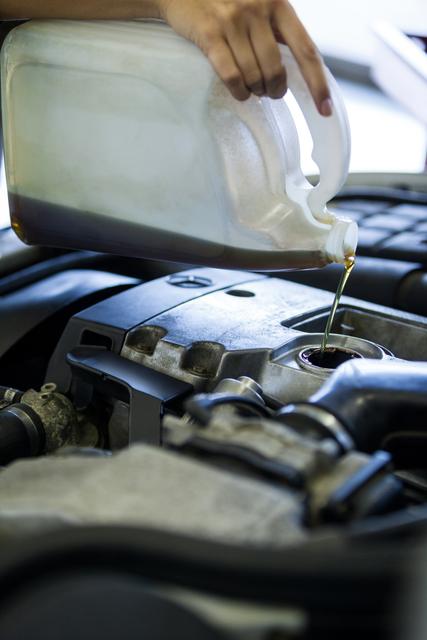 Mechanic pouring oil lubricant into car engine in a garage. Ideal for illustrating automotive maintenance, car repair services, and engine care. Useful for websites, blogs, and advertisements related to vehicle maintenance and repair services.