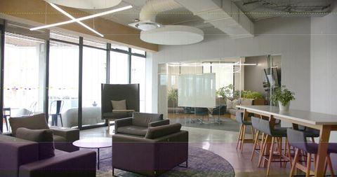 Coworking lounge featuring grey armchairs, purple rug, high-top table and glass meeting room