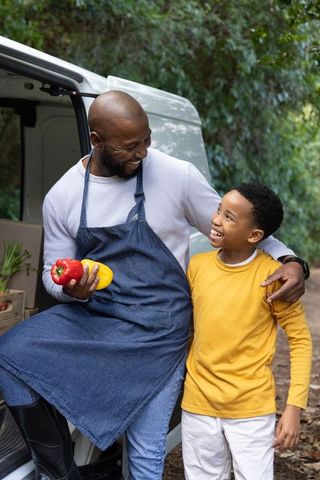 African american father and son selling fresh farm peppers from van market sharing joyful moment