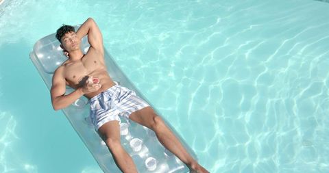 Young man relaxing on clear inflatable lounger in turquoise pool under summer sun