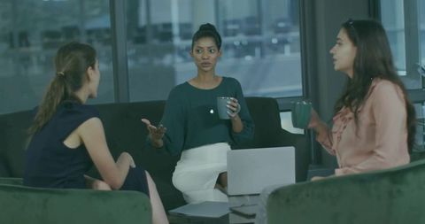 Woman leading team discussion in modern office lounge with laptop and coffee mugs