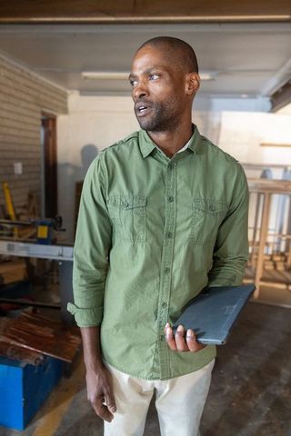 African american craftsman standing in workshop holding tablet inspecting wood frames