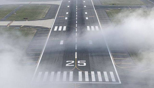 Foggy runway 25 with skid marks and centerline stretching toward horizon at airport