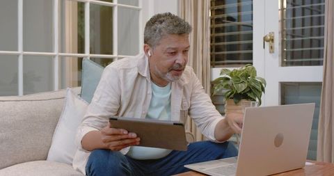 Senior Man Multitasking with Laptop and Tablet at Home