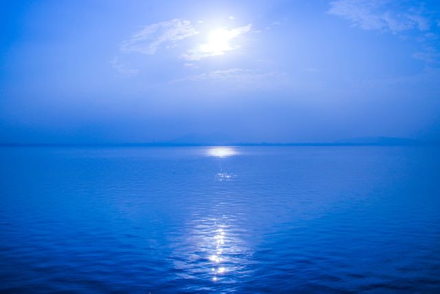 Serene scene of the ocean under a clear morning sky with the sun rising and casting reflections on the water. Ideal for use in travel publications, nature-themed articles, desktop backgrounds, or meditation apps. Promotes feelings of peace and tranquility.