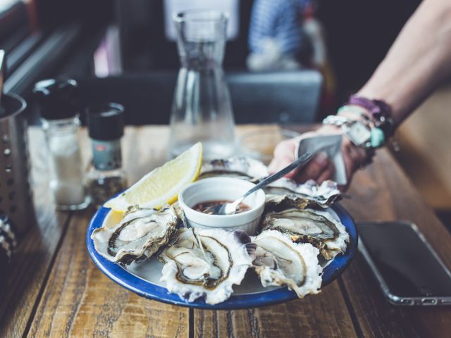 Plate of fresh oysters with lemon wedge and dipping sauce being served on rustic wooden table. Ideal for depicting premium dining, gourmet food experiences, seafood restaurants, culinary branding, and lifestyle blogs.