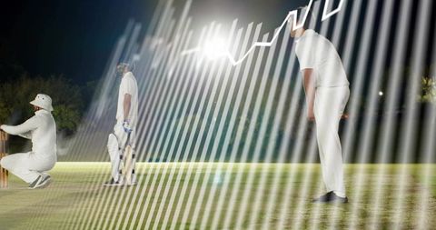 Night cricket action with bowler following through, batsman at crease under floodlights
