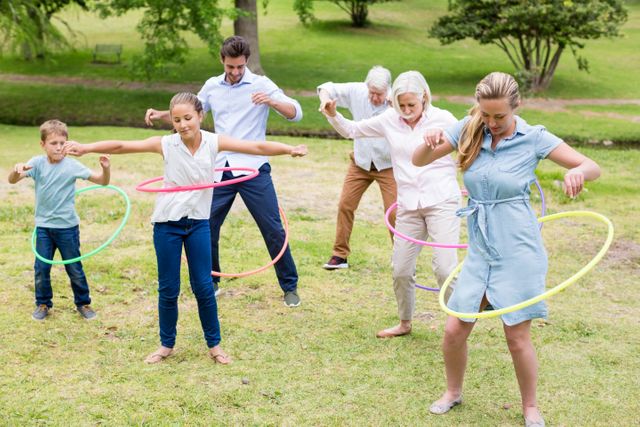 Scene of a multi-generation family engaging in a fun hula hoop activity in a park. Ideal for use in promoting family bonding activities, outdoor fitness programs, community events, and healthy lifestyle campaigns.