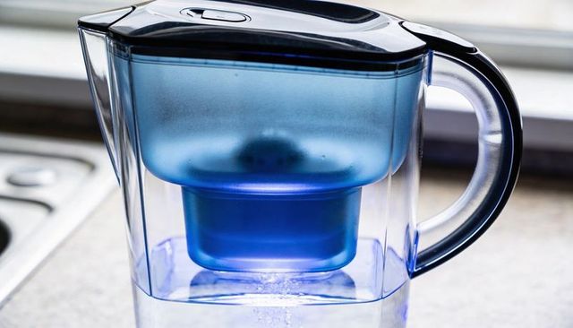 Filtering water with blue cartridge in transparent pitcher on kitchen countertop