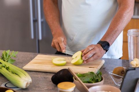 Mature man slicing green apple on cutting board for healthy meal prep in modern kitchen