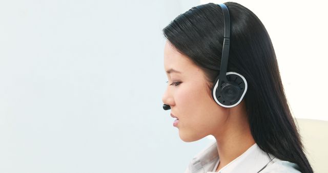 Portrait of asian businesswoman using headphones in office with copy space. Business, office, work and professionals concept, unaltered.