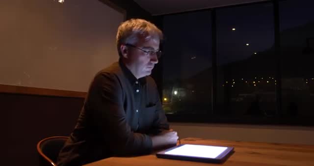 Caucasian man using a tablet at night in a creative office setting. He appears to be interacting with a 3D object or hologram, showing innovation and futuristic technology. Useful for concepts like modern work environments, late-night productivity, tech innovations, and business presentations.