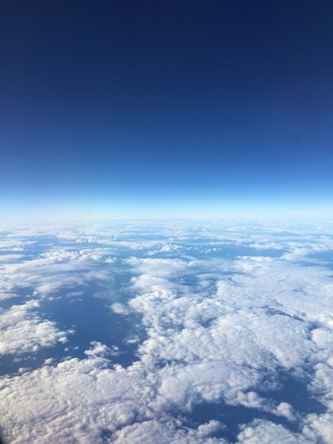 View shows expansive cloud formations from airplane window under clear blue sky, evoking feelings of travel, freedom, and serenity. Featuring a peaceful scene ideal for travel blogs, websites, backgrounds, or motivational content promoting travel and inspiration.