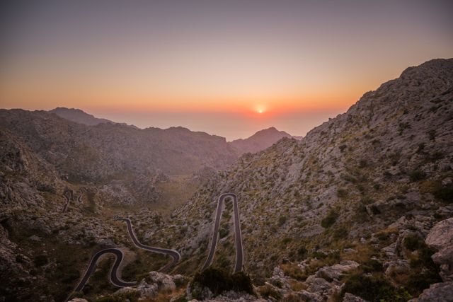 Winding mountain road with rocky surroundings during sunset in Mallorca. Ideal for travel and tourism websites, adventure blogs, nature photography collections, postcards, and scenic backgrounds for promotions or presentations.