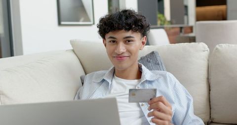 Young Man Shopping Online With Credit Card On Sofa