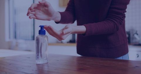 Woman dispensing hand sanitizer in modern kitchen