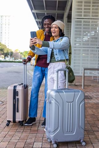 Young diverse couple taking selfie with luggage at train station platform
