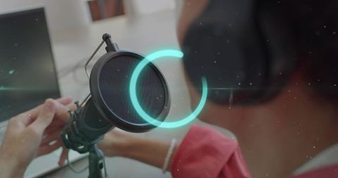 Podcaster adjusting studio microphone with pop filter and headphones in home workspace