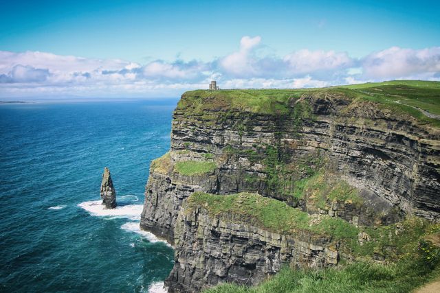 Cliffs of Moher, located on the western coast of Ireland, under bright blue sky with rugged cliffs plunging into the Atlantic Ocean. This picturesque location is perfect for promoting tourism, travel magazines, nature documentaries, or educational content about natural landmarks and geography.