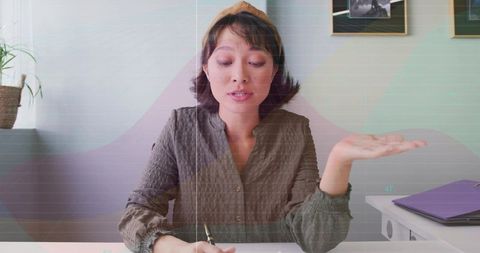 Young woman writing notes while explaining with gesture at minimalist home workspace