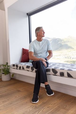 Senior man gazing from cozy window seat with mountain view while checking watch