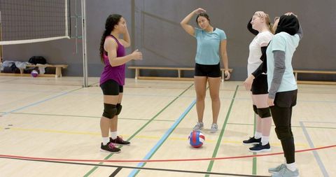 Diverse female volleyball team huddling and planning drills during indoor training