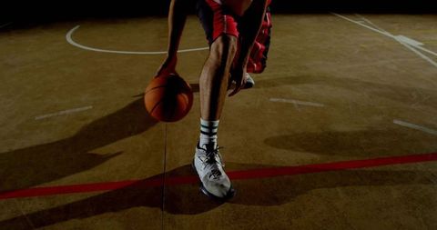 Low dribble basketball player on indoor court with red shorts and dramatic shadow