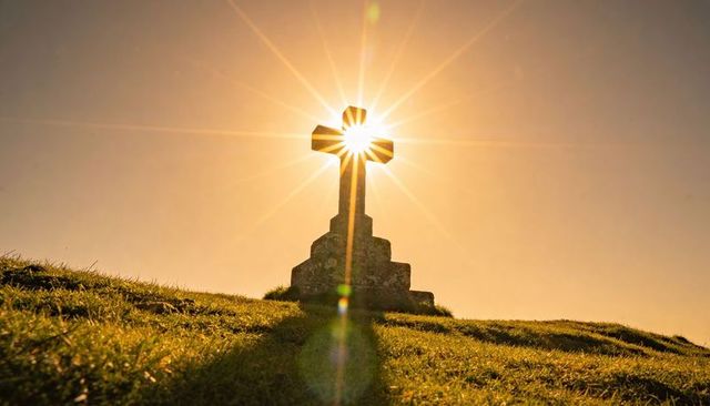 Sunburst cross silhouette on hilltop casting long shadow during golden hour