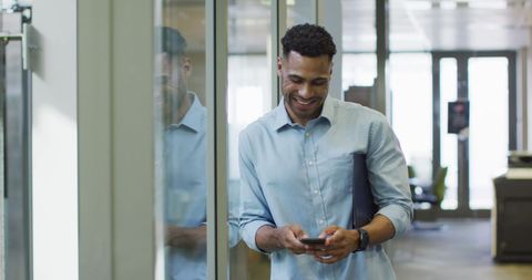 Smiling Businessman Engages with Smartphone in Bright Office Space