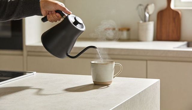 Minimalist morning pouring with black gooseneck kettle into ceramic mug on kitchen island