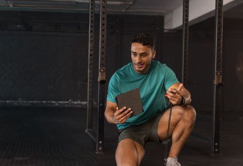Coaching client using tablet and jump rope in industrial gym with teal workout shirt