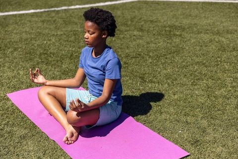 African american child meditating cross-legged on pink yoga mat outdoors on green turf