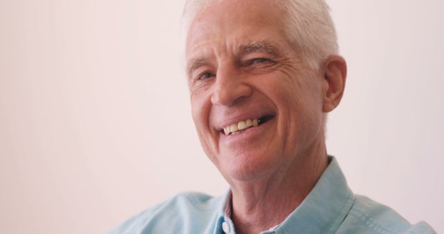 Cheerful elder man with grey hair wearing light blue shirt and smiling warmly. Ideal for themes emphasizing positivity, senior wellbeing, aging happily, or lifestyle content geared towards older adults.