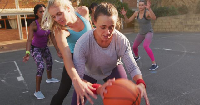 Diverse female basketball team playing match, dribbling ball and scoring goal. basketball, sports training at an outdoor urban court.