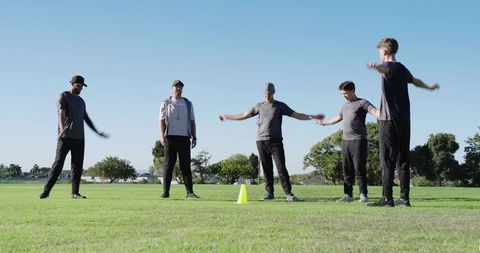 Male athletes warming up performing arm circles and overhead stretches around cone in park