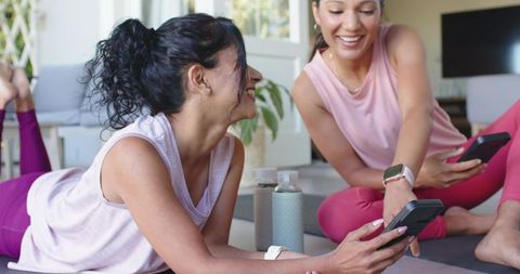 Sharing smartphone workout tips during home yoga session with friends in pastel activewear