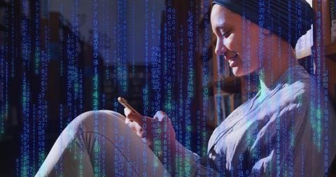 Young woman wearing turban scrolling smartphone on couch with futuristic numeric code overlay