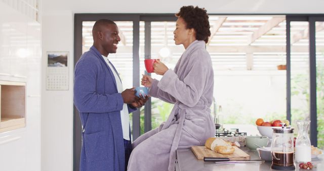 Young couple enjoys morning coffee together in a modern kitchen. Scene showcases a intimate, relaxed domestic setting with both individuals in bathrobes, creating a cozy and warm atmosphere. Ideal for lifestyle promotions, couple bonding themes, morning routines, and home life marketing material.